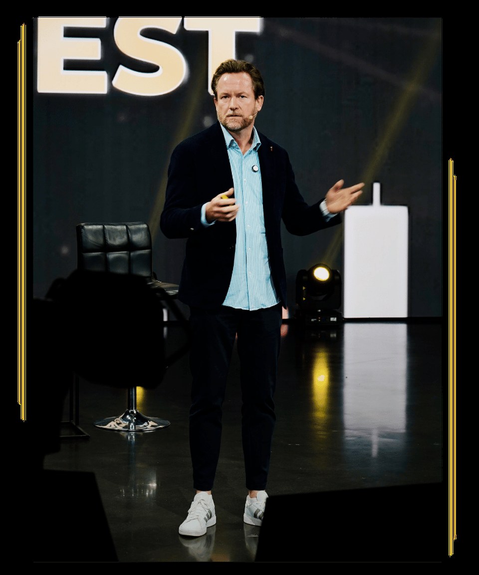Markus Miller steht redend auf einer Bühne vor einem großen INVEST-Schriftzug